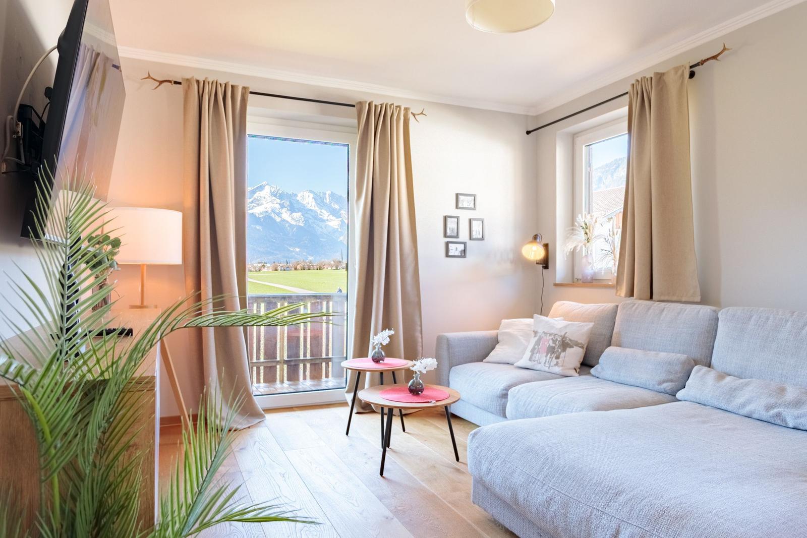 Wohnzimmer mit Sofa, TV und Balkonblick auf Berge
