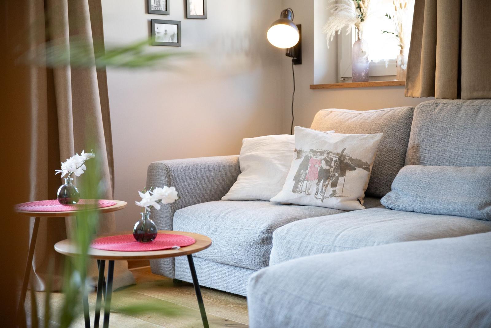 Ein grauer Sofa mit Kissen, zwei runde Tische und eine Wandlampe.