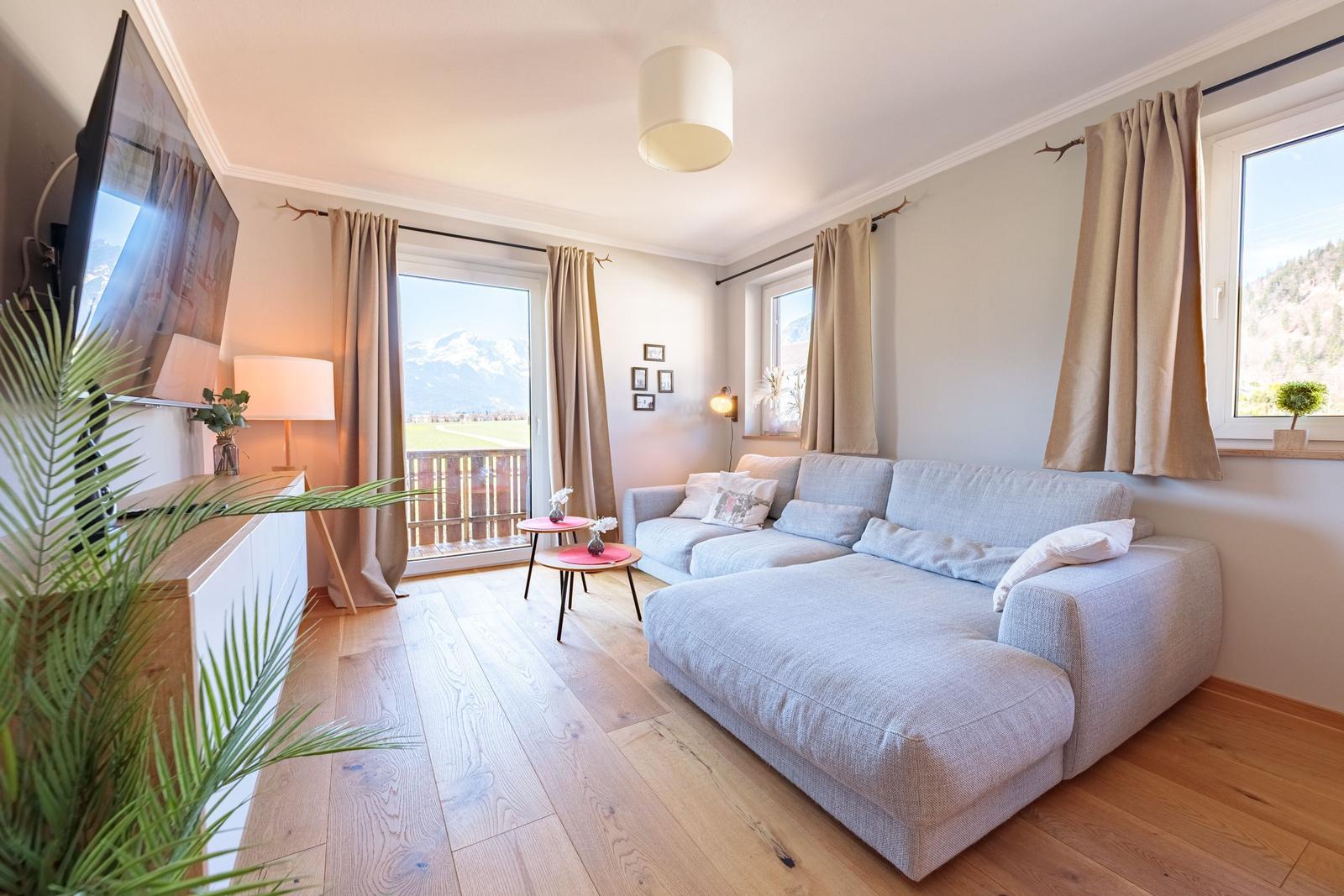 Wohnzimmer mit Sofa, Fernseher und Balkonblick auf Berge.