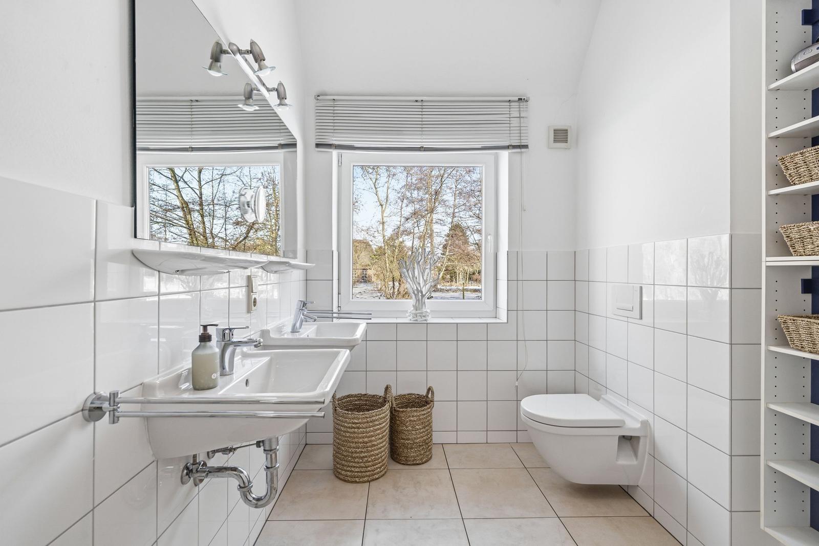 Badezimmer mit Waschbecken, Toilette und Fenster mit Blick auf Bäume.