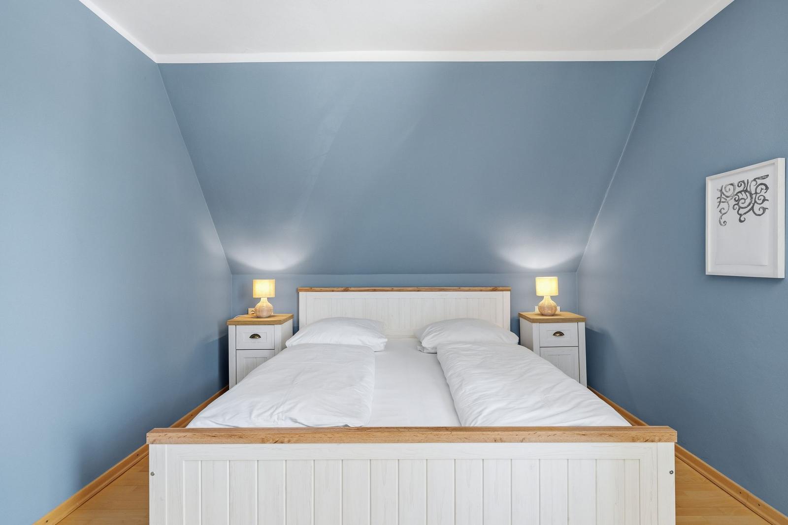 Schlafzimmer mit Doppelbett, zwei Nachttischen und blauen Wänden.