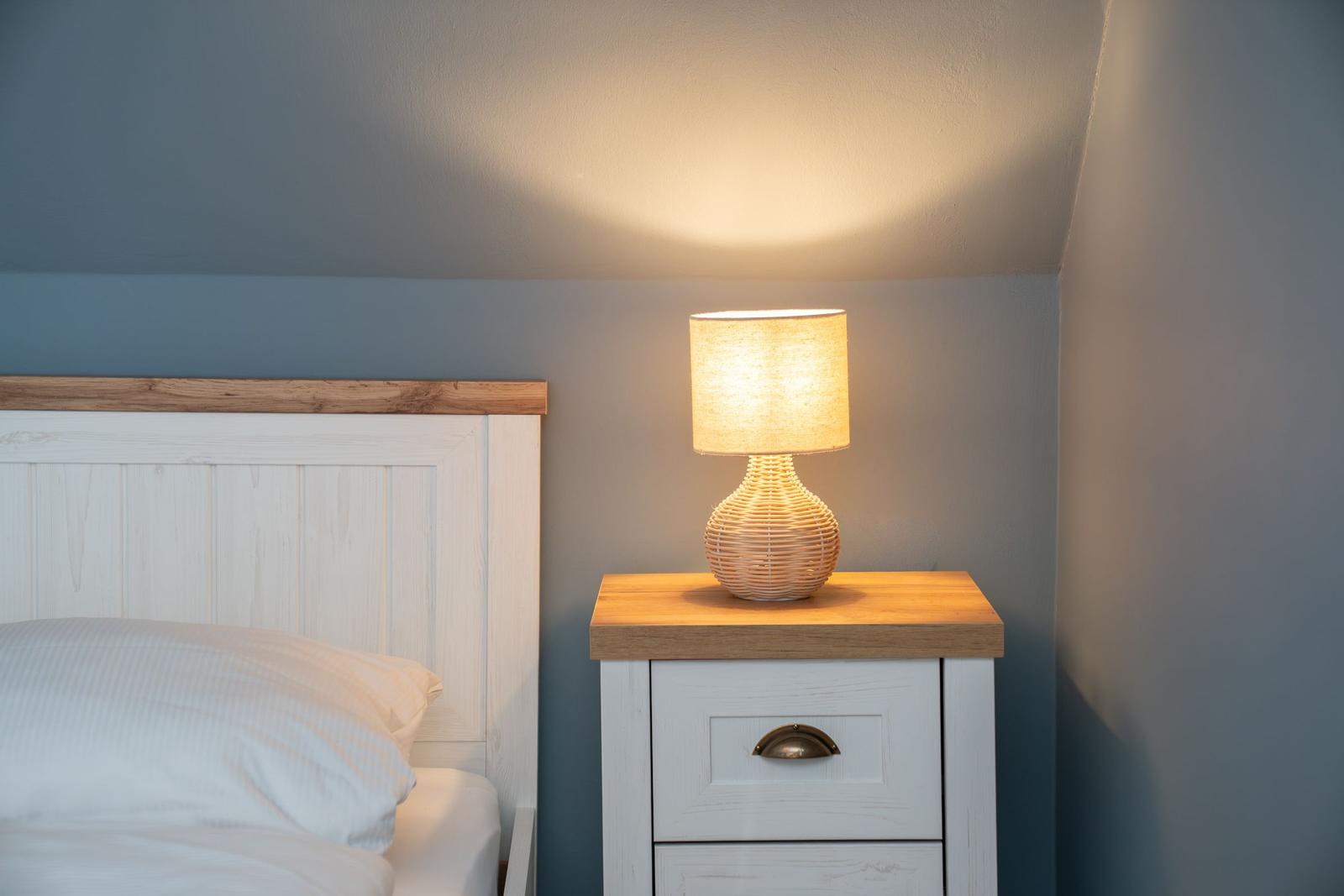 Bettkopfteil mit Holzrahmen, Nachttisch mit Schublade und Lampe mit geflochtenem Schirm.