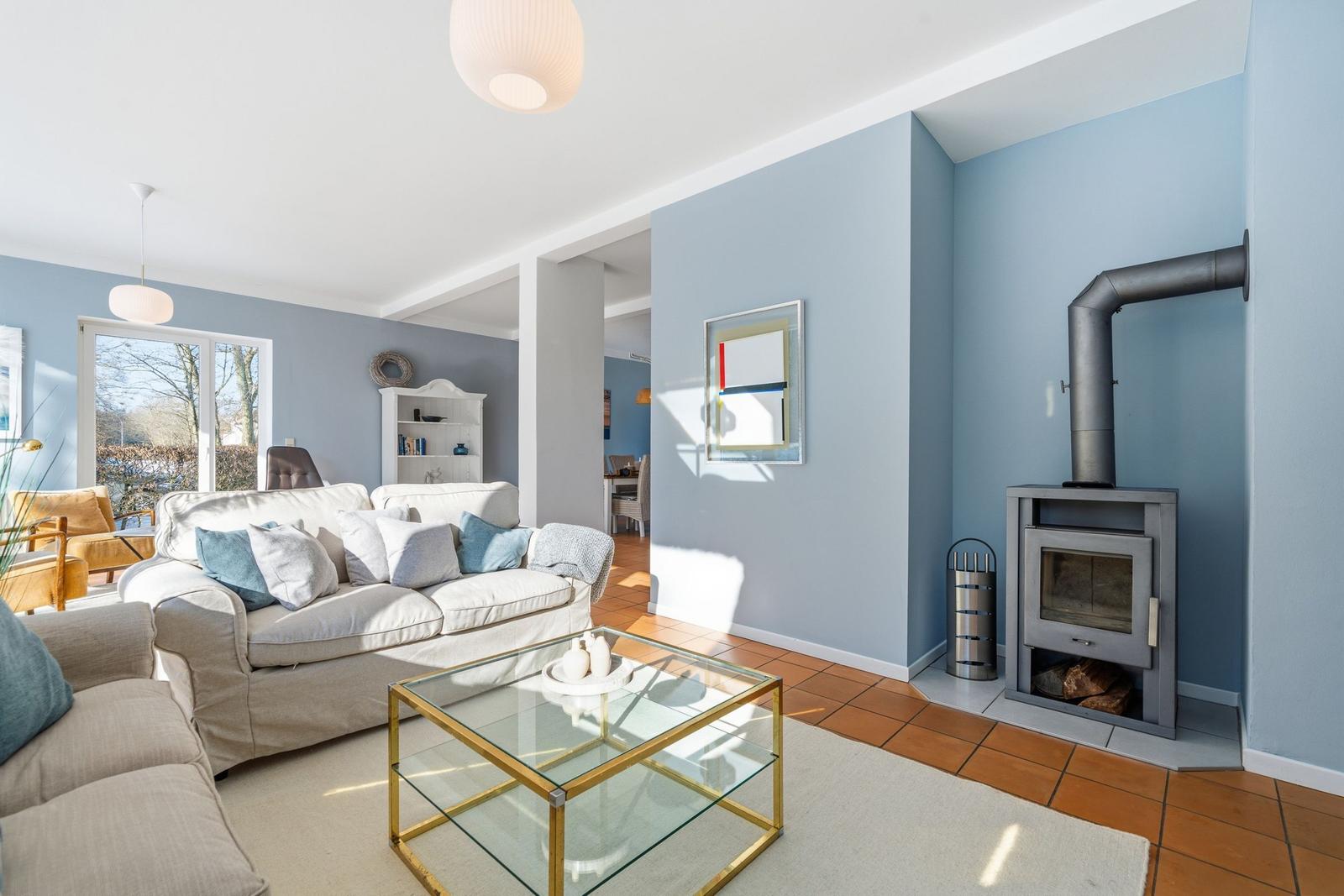 Wohnzimmer mit Sofa, Glas-Tisch und Kaminofen an blauen Wänden.