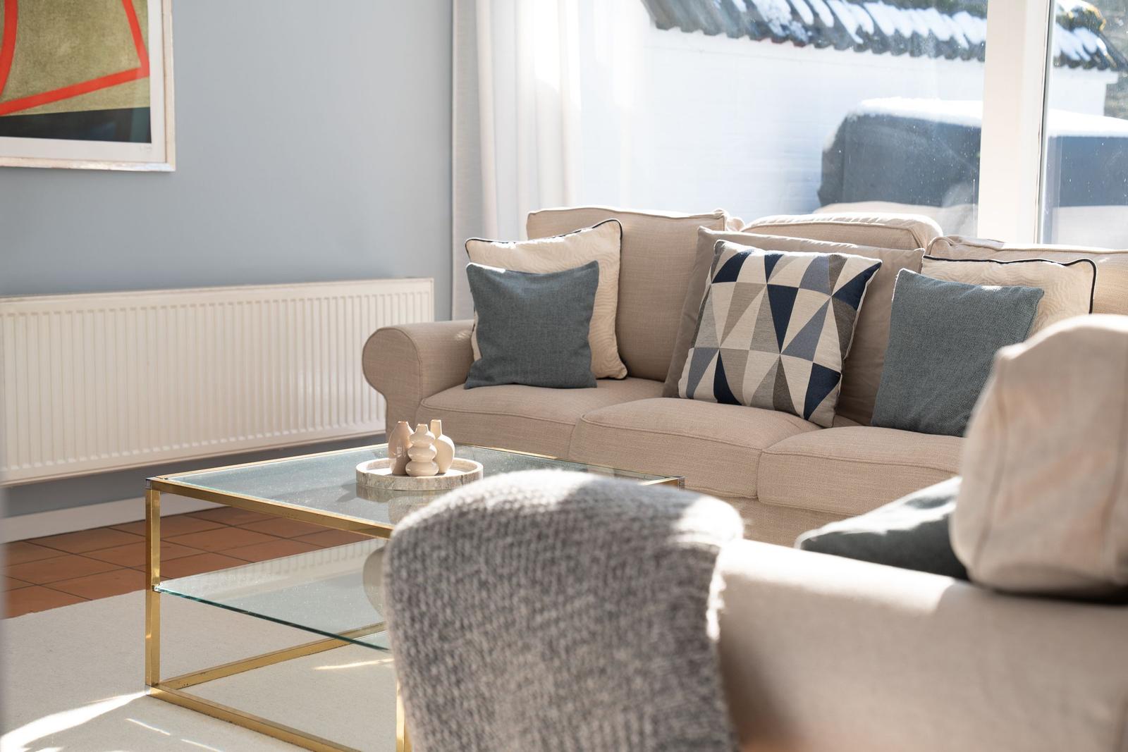 Ein Wohnzimmer mit Sofa, Kissen und Glas-Tisch. Fenster zeigt Schnee.