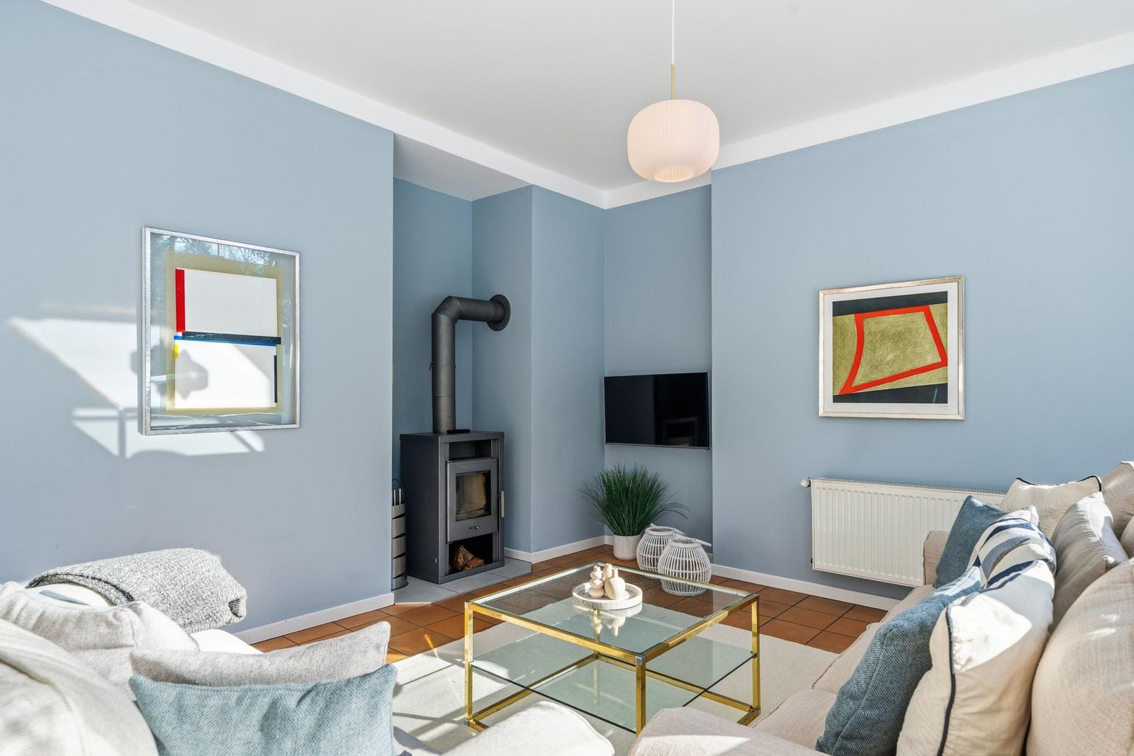 Wohnzimmer mit Sofa, Glas-Tisch und Kaminofen an der Wand.