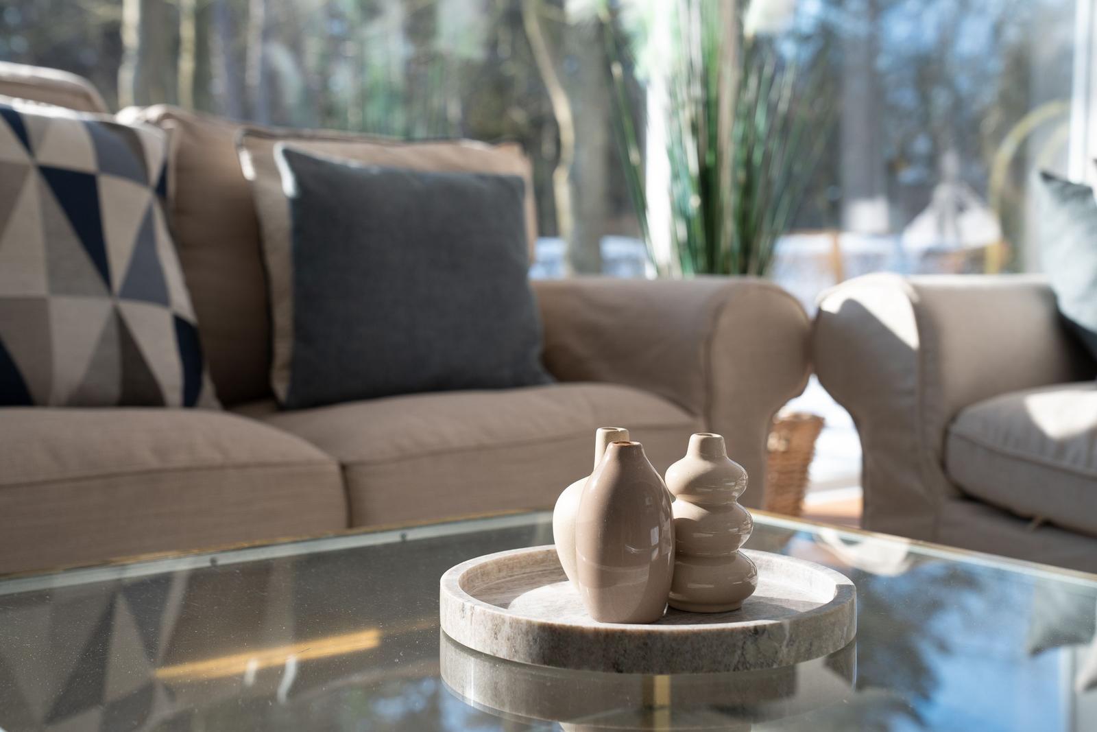 Ein Wohnbereich mit einem Sofa, Kissen und einer Glasplatte mit Vasen.