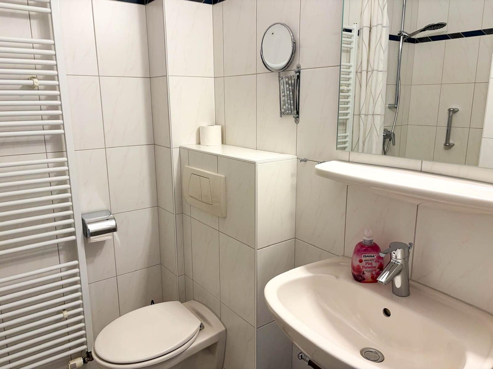 Badezimmer mit Toilette, Waschbecken und Dusche. Weiße Fliesen und Spiegel.