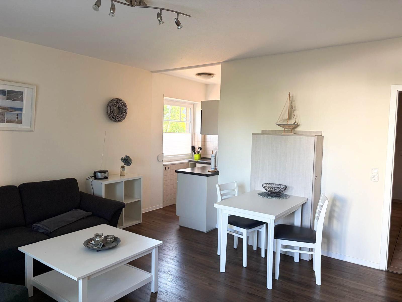 Wohn- und Essbereich mit Sofa, Esstisch und Küchenzeile. Holzboden und helle Wände.