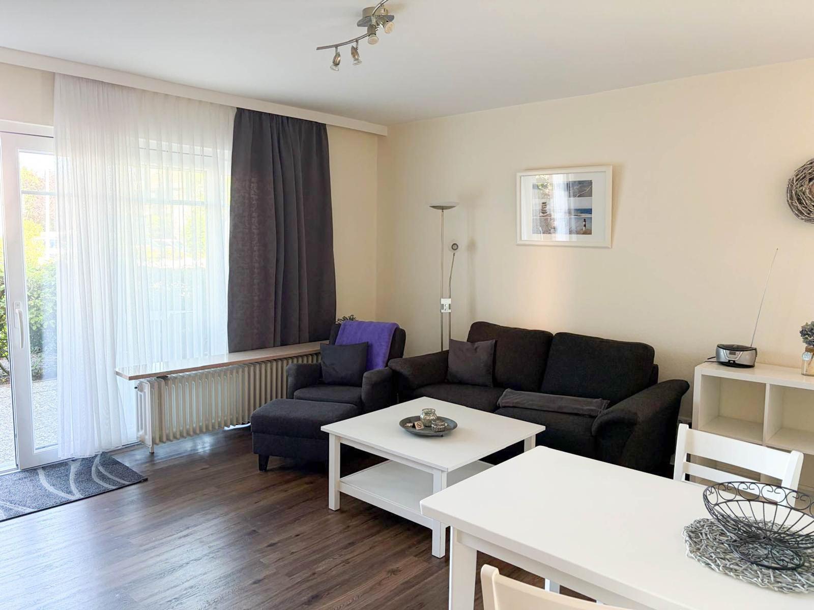 Wohn- und Essbereich mit Sofa, Tisch und Fenster. Holzboden und weiße Möbel.