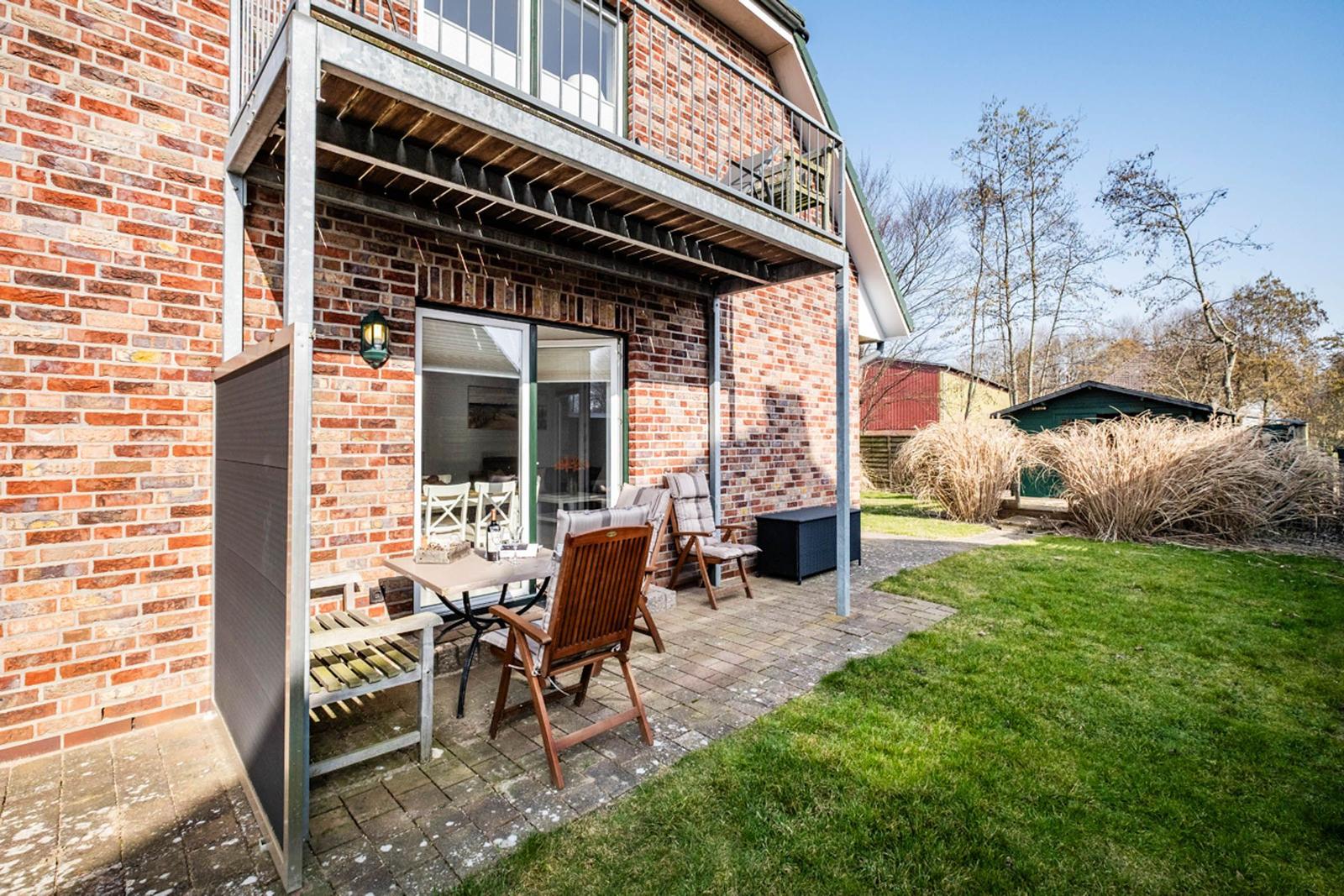 Terrasse mit Tisch und Stühlen an einem Backsteinhaus mit Balkon.