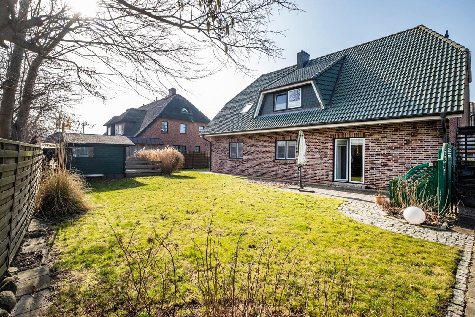 Haus mit Garten, Terrasse und grünem Rasen. Hinterhof mit Holzzaun und Pflanzen.