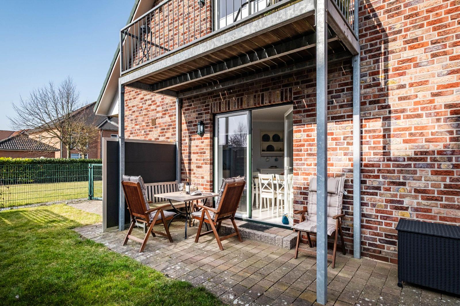 Terrasse mit Tisch, Stühlen und Sitzbank. Glasfront öffnet sich ins Innere. Hinterhof mit Rasen.