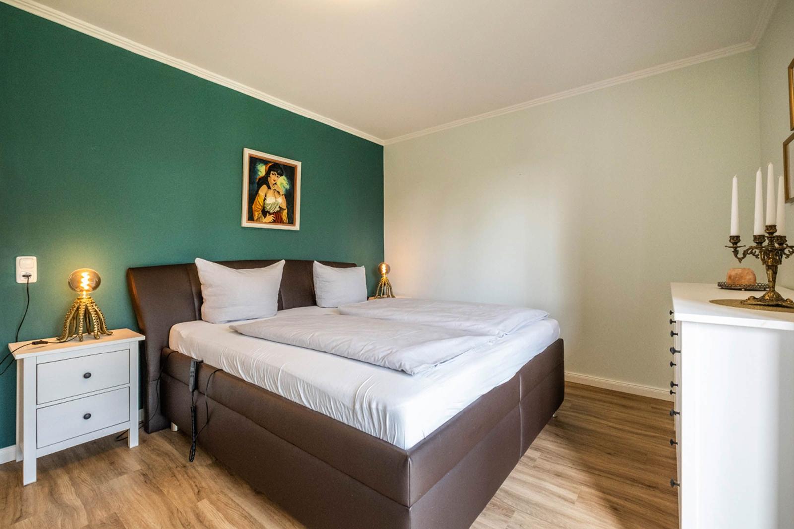 Schlafzimmer mit Bett, Nachttisch und Wandbild. Holzboden und grüne Wand.