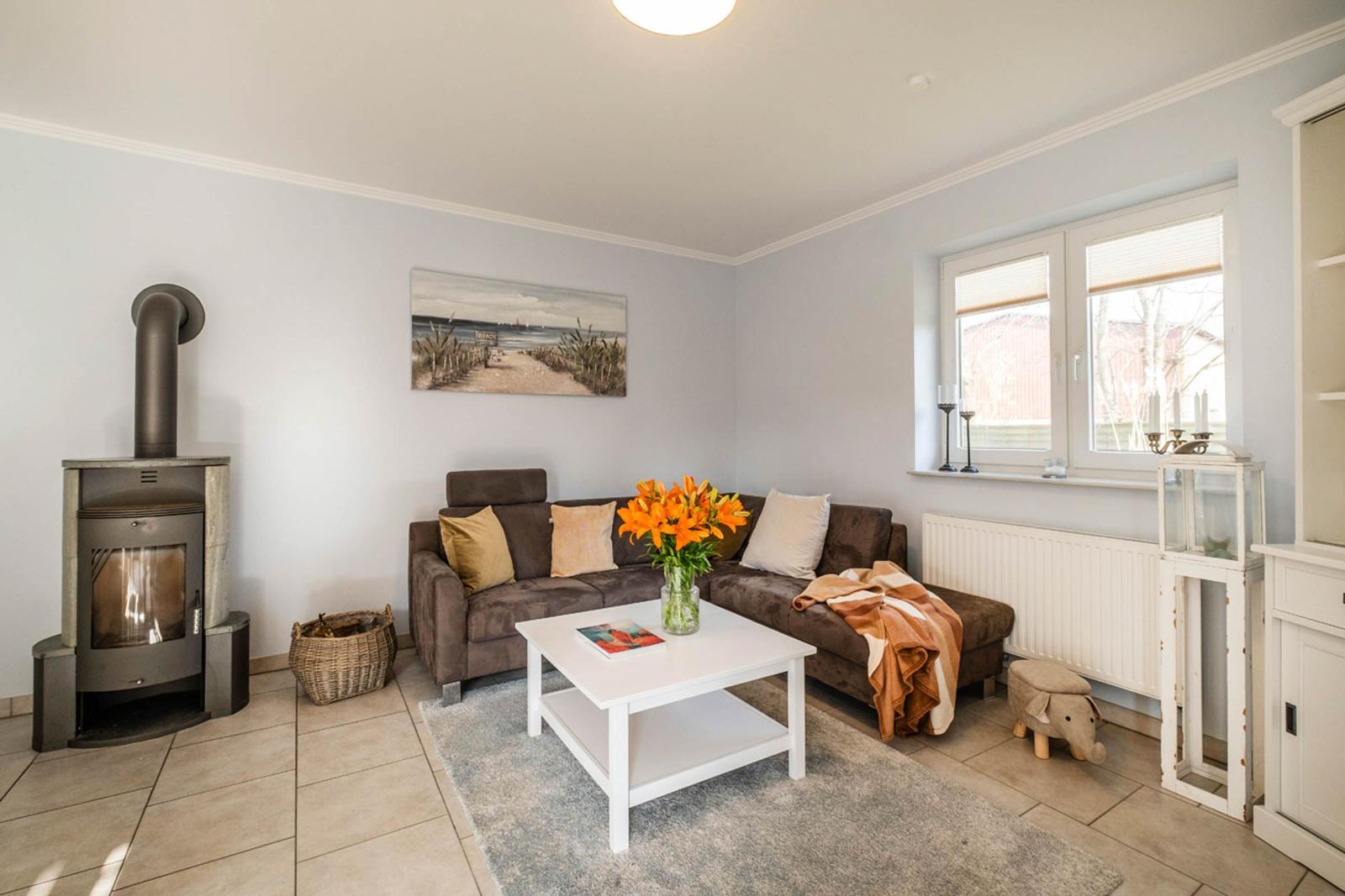 Wohnzimmer mit Sofa, Kamin und Fenster. Tisch mit Blumen und Teppich.
