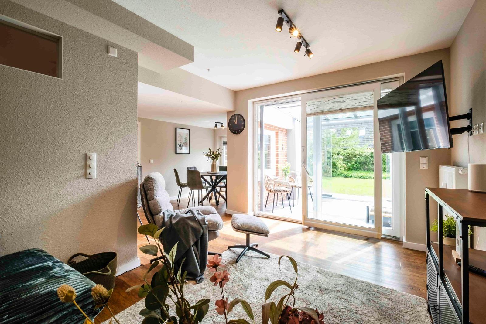 Wohnbereich mit Sessel, Fernseher und Blick auf die Terrasse.