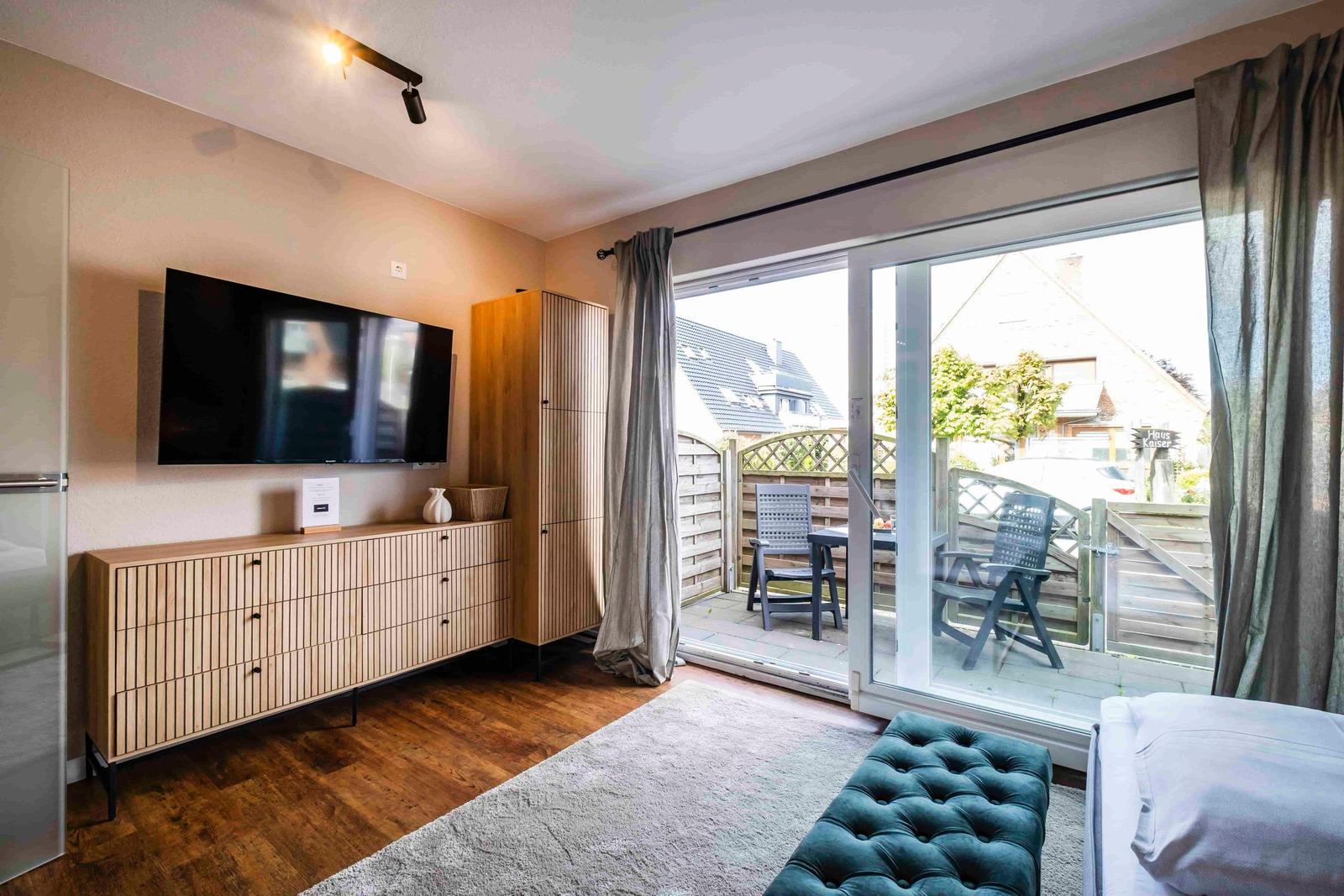 Wohnzimmer mit TV, Holzmöbel und Balkon mit Sitzgelegenheiten.