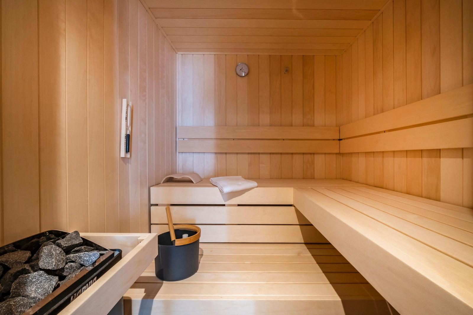Sauna mit Holzbänken, Steinen und Eimer. Thermometer an der Wand.
