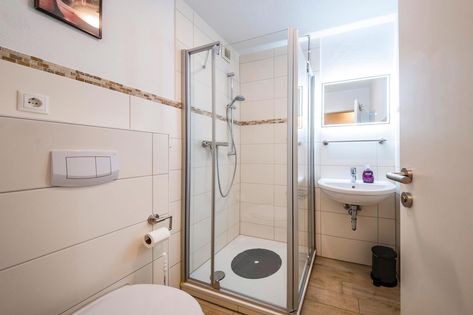 Badezimmer mit Dusche, Waschbecken und Toilette. Fliesenwand und Holzboden.