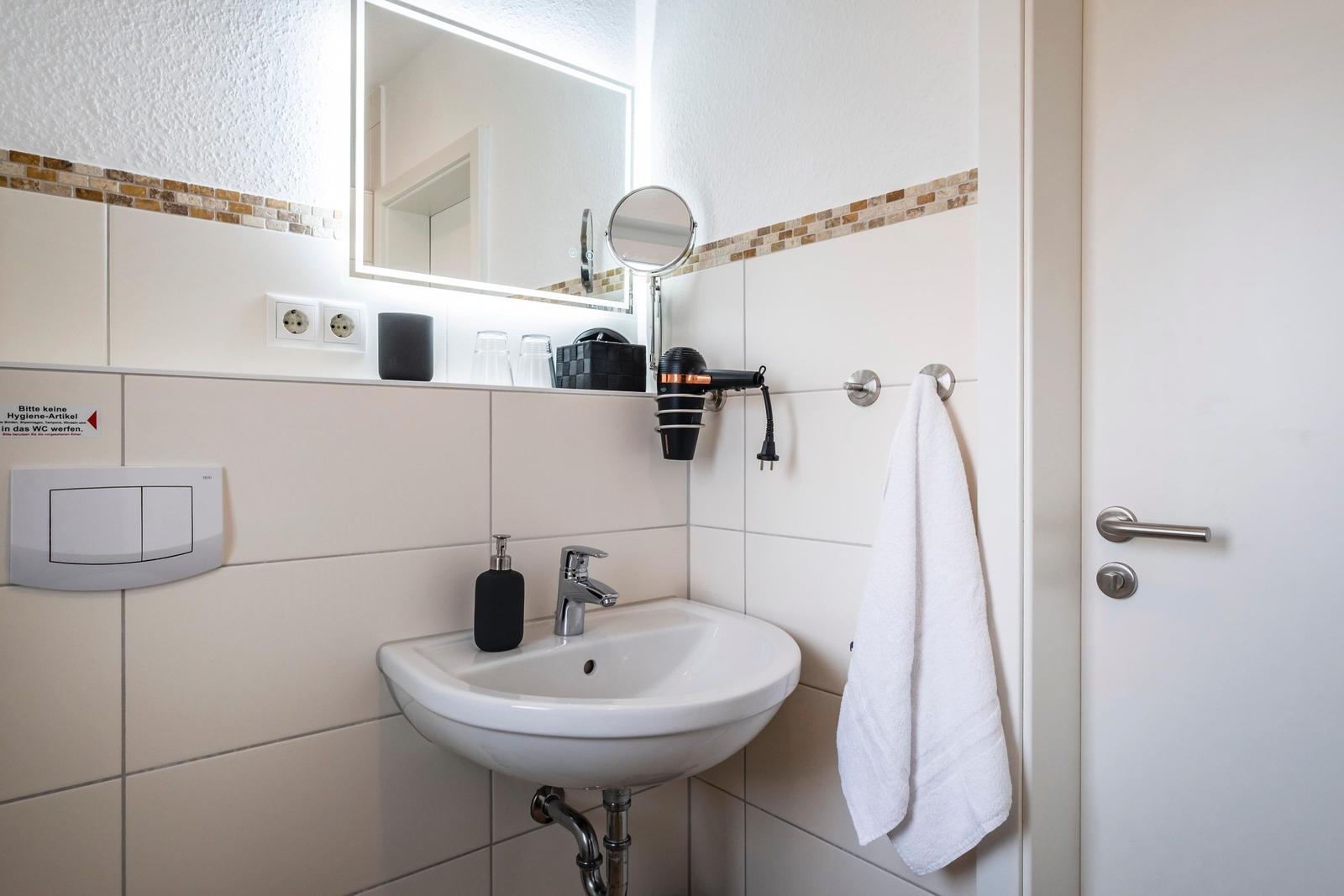 Badezimmer mit Waschbecken, Spiegel und Handtuchhalter.