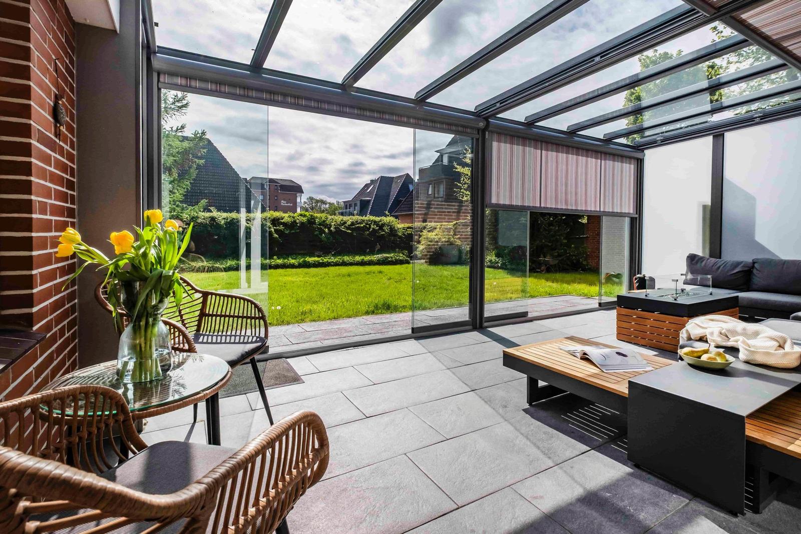 Terrasse mit Glasdach, Sitzgruppe und Blick auf den Garten.