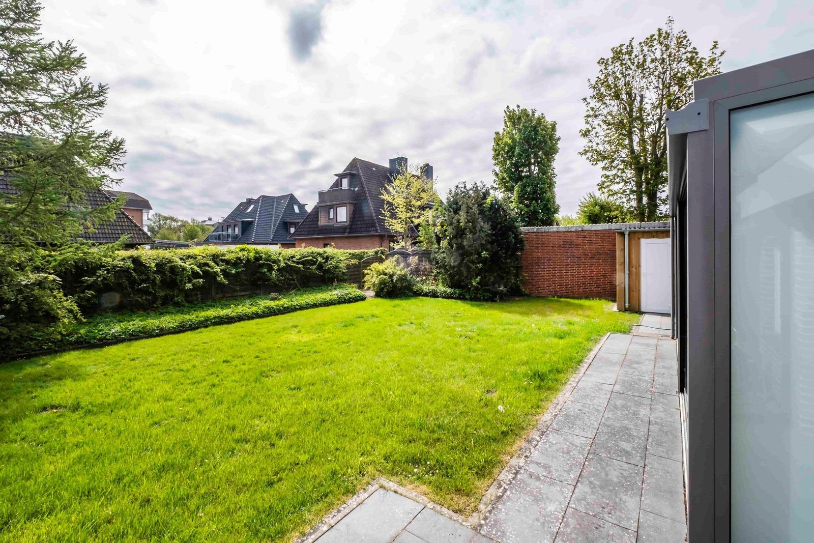 Hinterhof mit grünem Rasen, gepflastertem Weg und Gartenzaun. Im Hintergrund sind Häuser zu sehen.