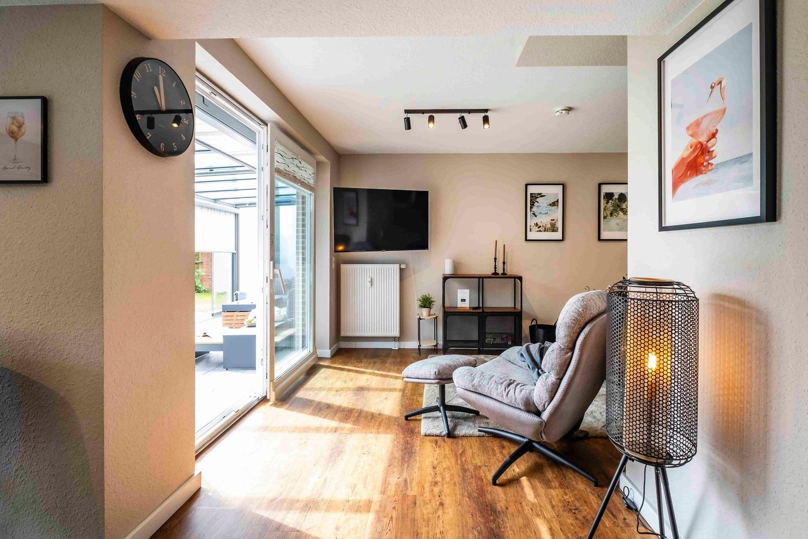 Wohnzimmer mit Sessel, Fernseher und Glasfront zur Terrasse.