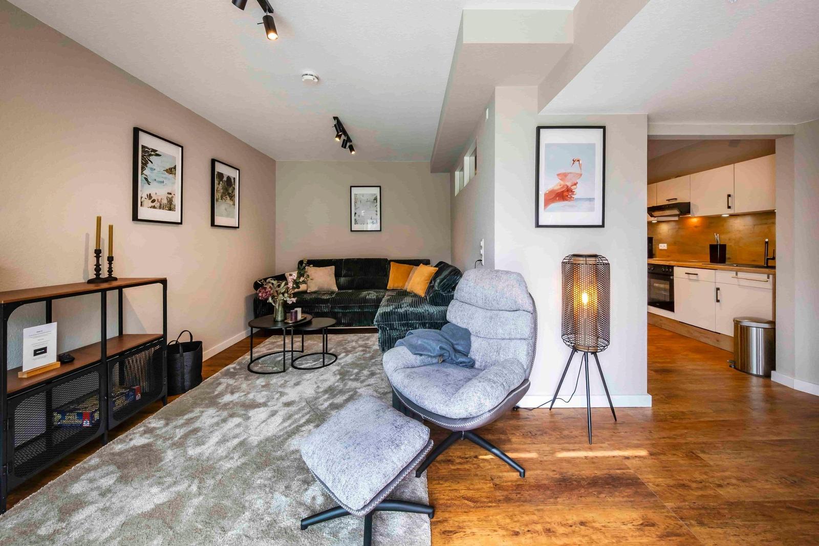 Wohnzimmer mit Sofa, Sessel und Küchenbereich im Hintergrund.