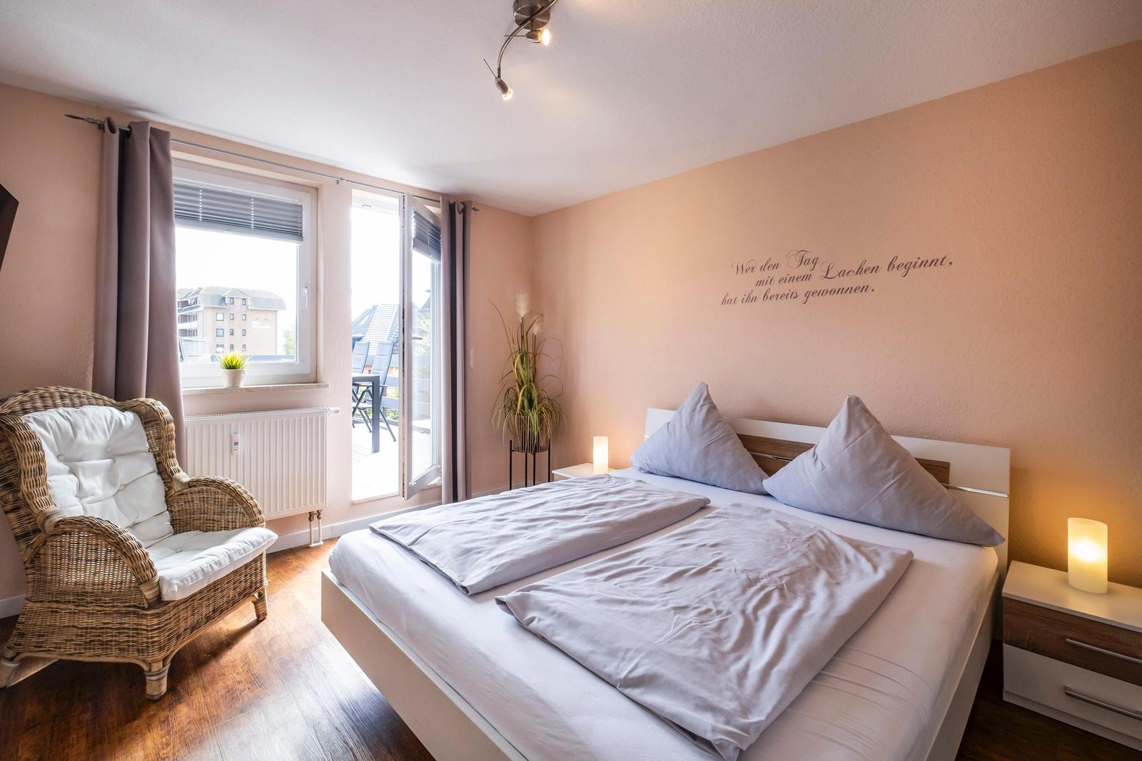 Schlafzimmer mit Bett, Sessel und Balkonzugang.