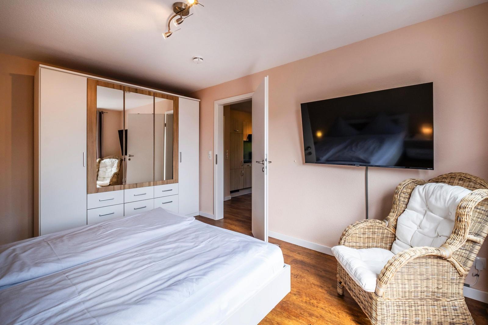 Schlafzimmer mit Bett, Kleiderschrank und Fernseher an der Wand.