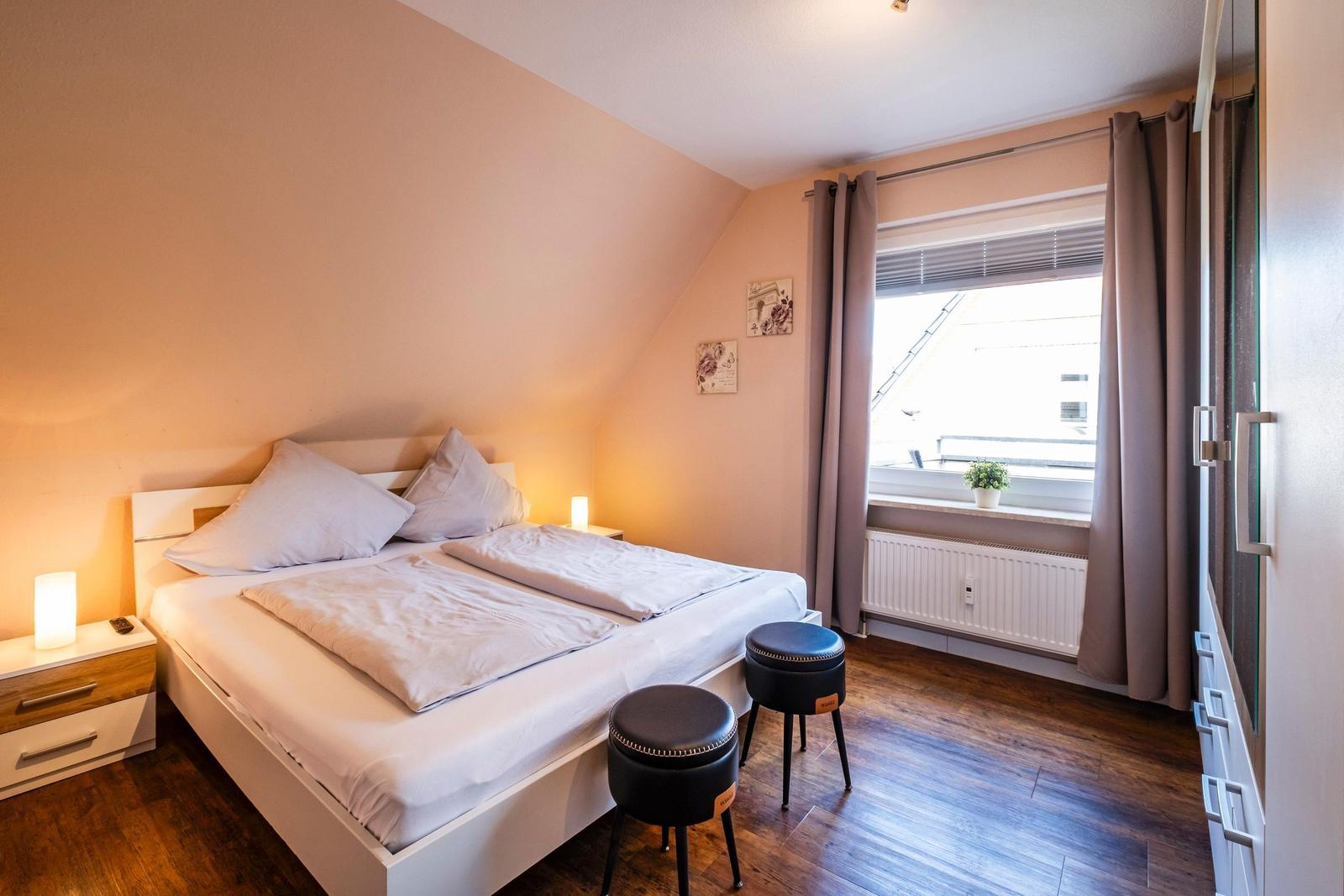 Schlafzimmer mit Doppelbett, zwei Nachttischen und Fenster mit Vorhängen.