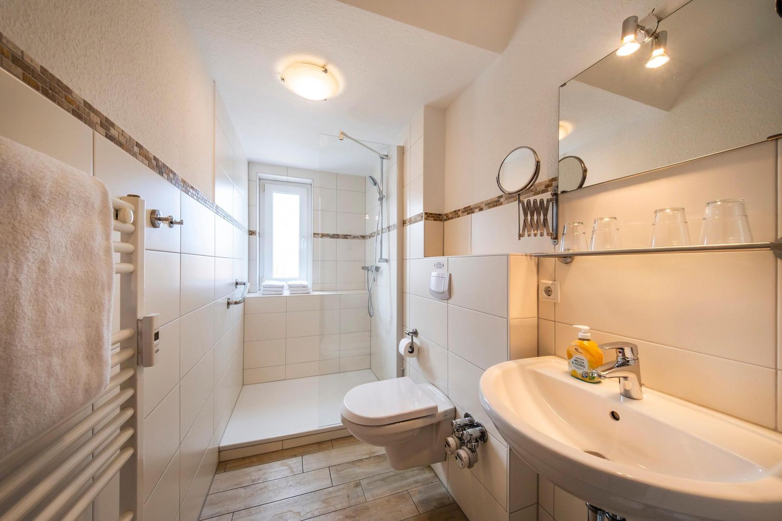 Badezimmer mit Dusche, Toilette und Waschbecken. Handtuchhalter und Spiegel sind vorhanden.