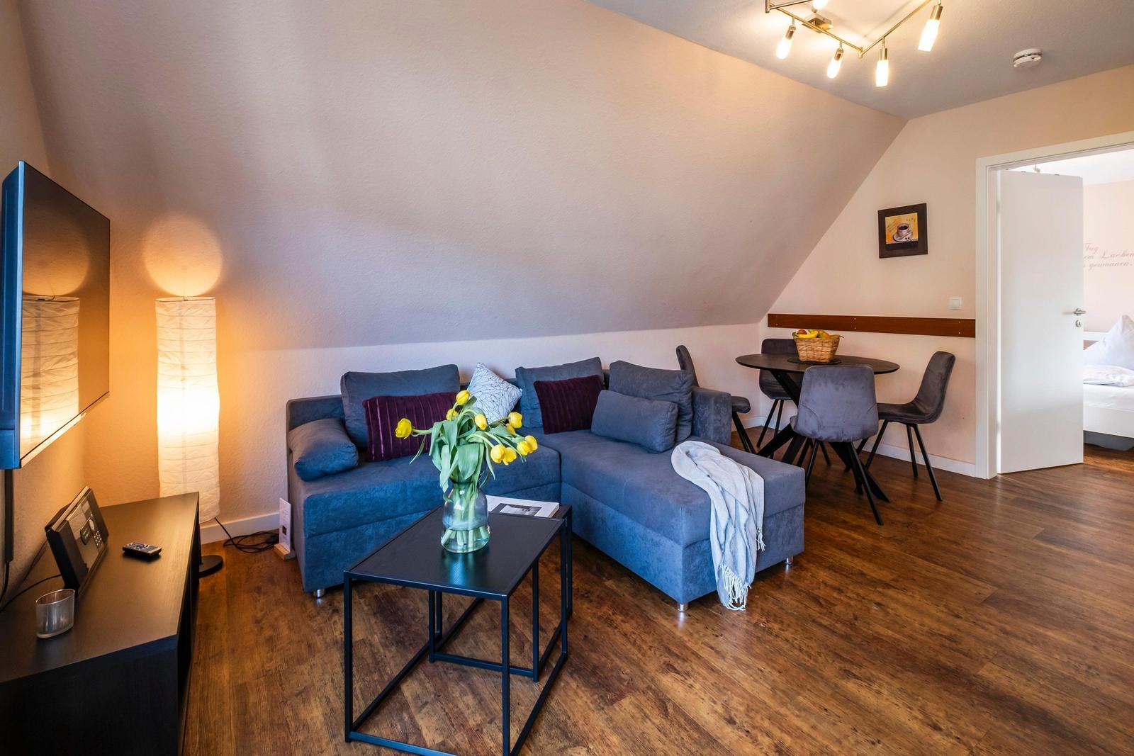 Wohnzimmer mit Sofa, Tisch und Fernseher. Holzboden und schräge Decke.