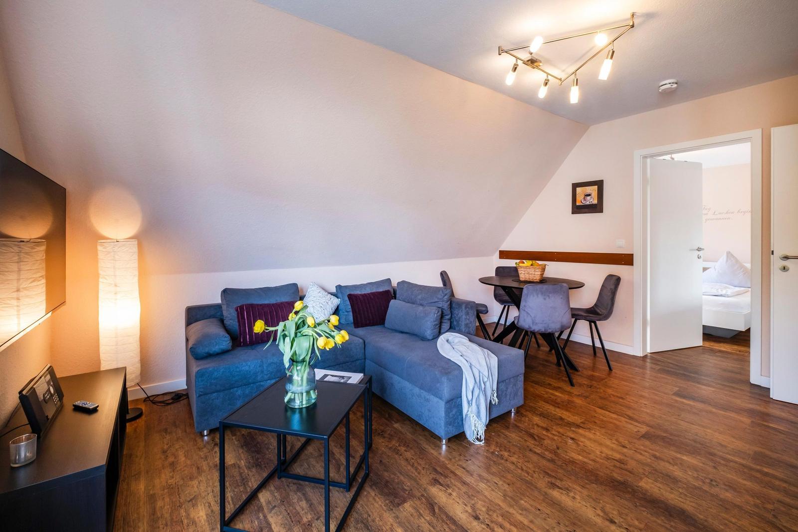 Wohnzimmer mit Sofa, Esstisch und Schlafzimmer im Hintergrund.