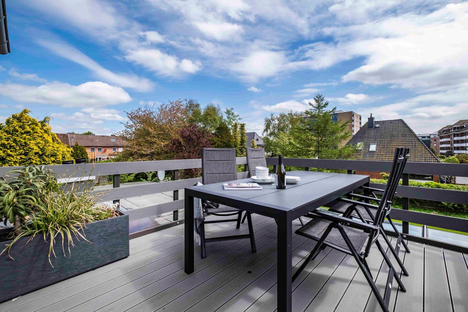 Terrasse mit Tisch, Stühlen und Pflanzen. Blick auf Wohngebiet und Bäume.