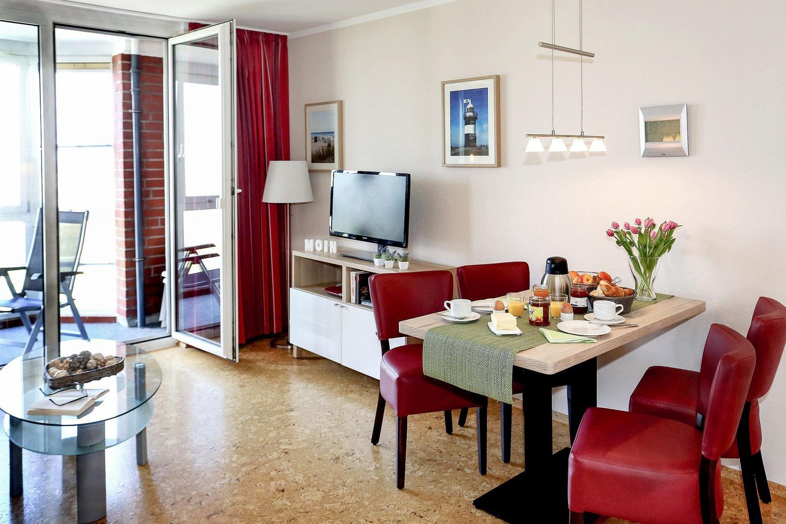 Essbereich mit Tisch, Stühlen und Frühstück. Wohnbereich mit TV und Balkontür.