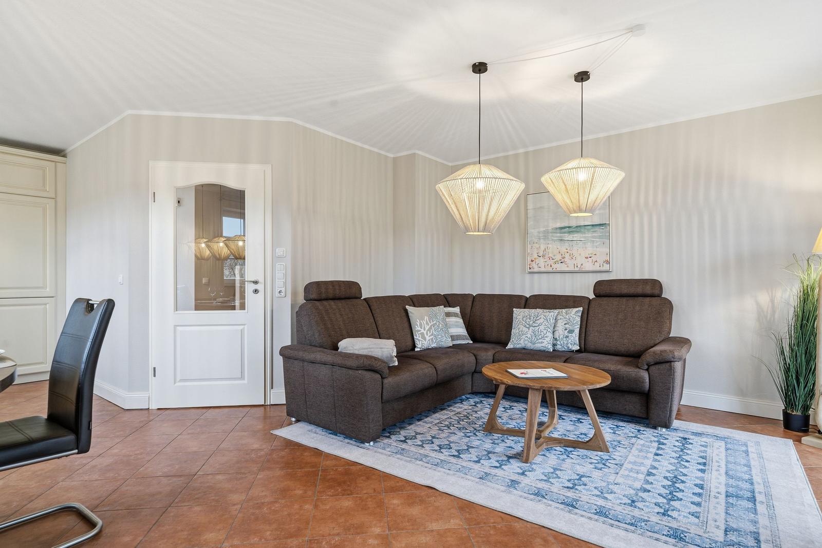 Wohnzimmer mit braunem Sofa, blauem Teppich und zwei hängenden Lampen.