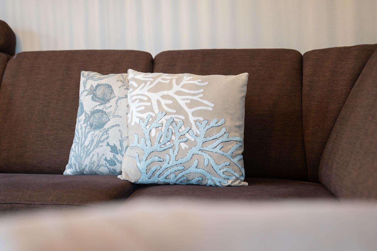 Zwei Kissen mit Korallenmustern auf einem braunen Sofa.