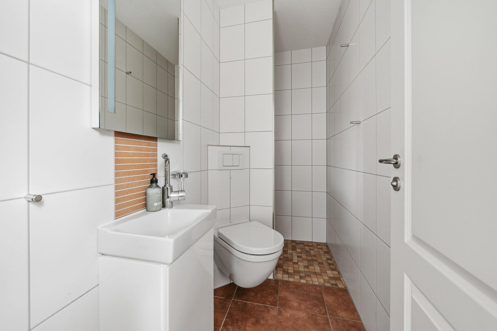 Badezimmer mit Waschbecken, Spiegel, WC und Dusche. Bodenfliesen und Wandfliesen.