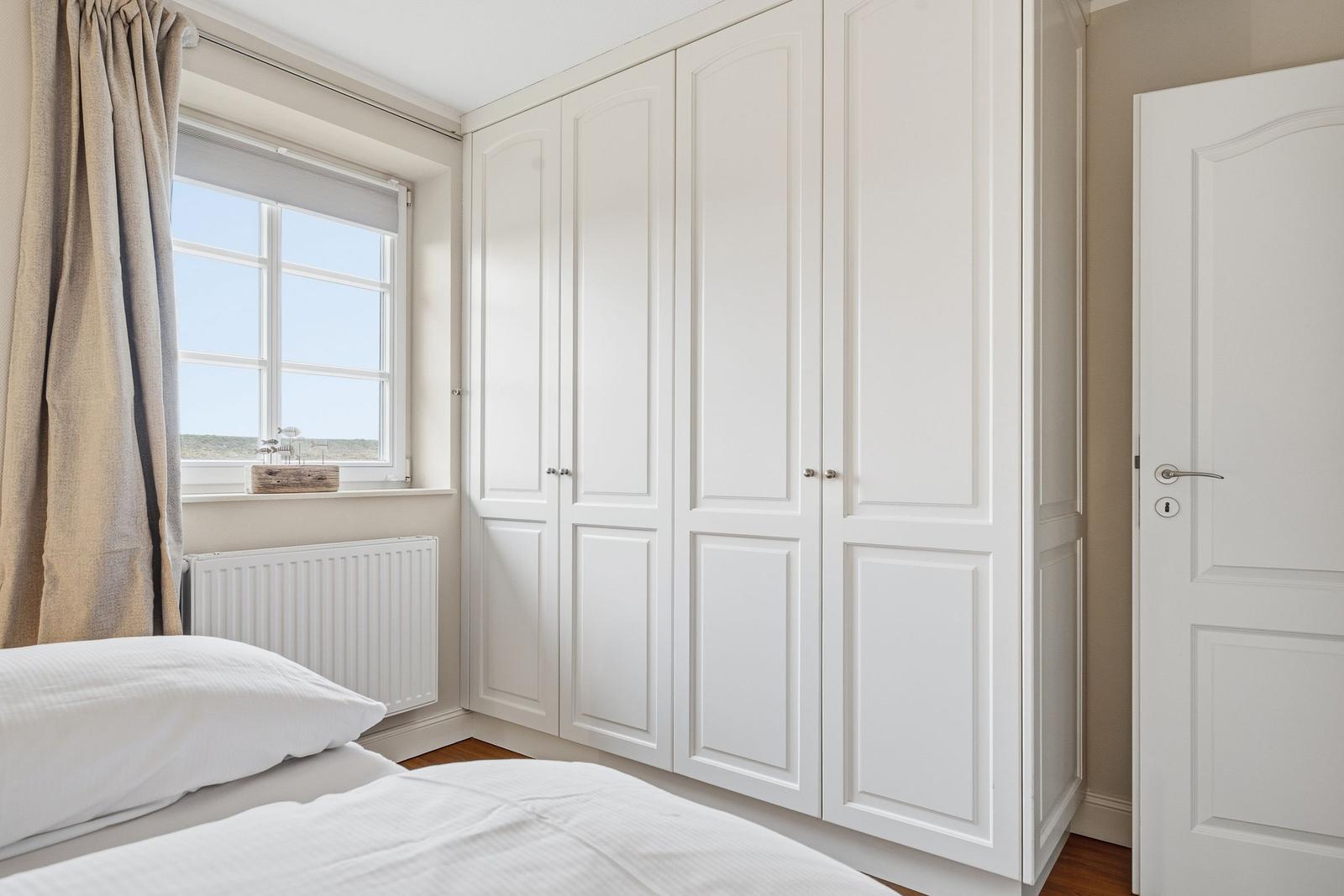 Schlafzimmer mit weißem Schrank, Fenster und Bett.