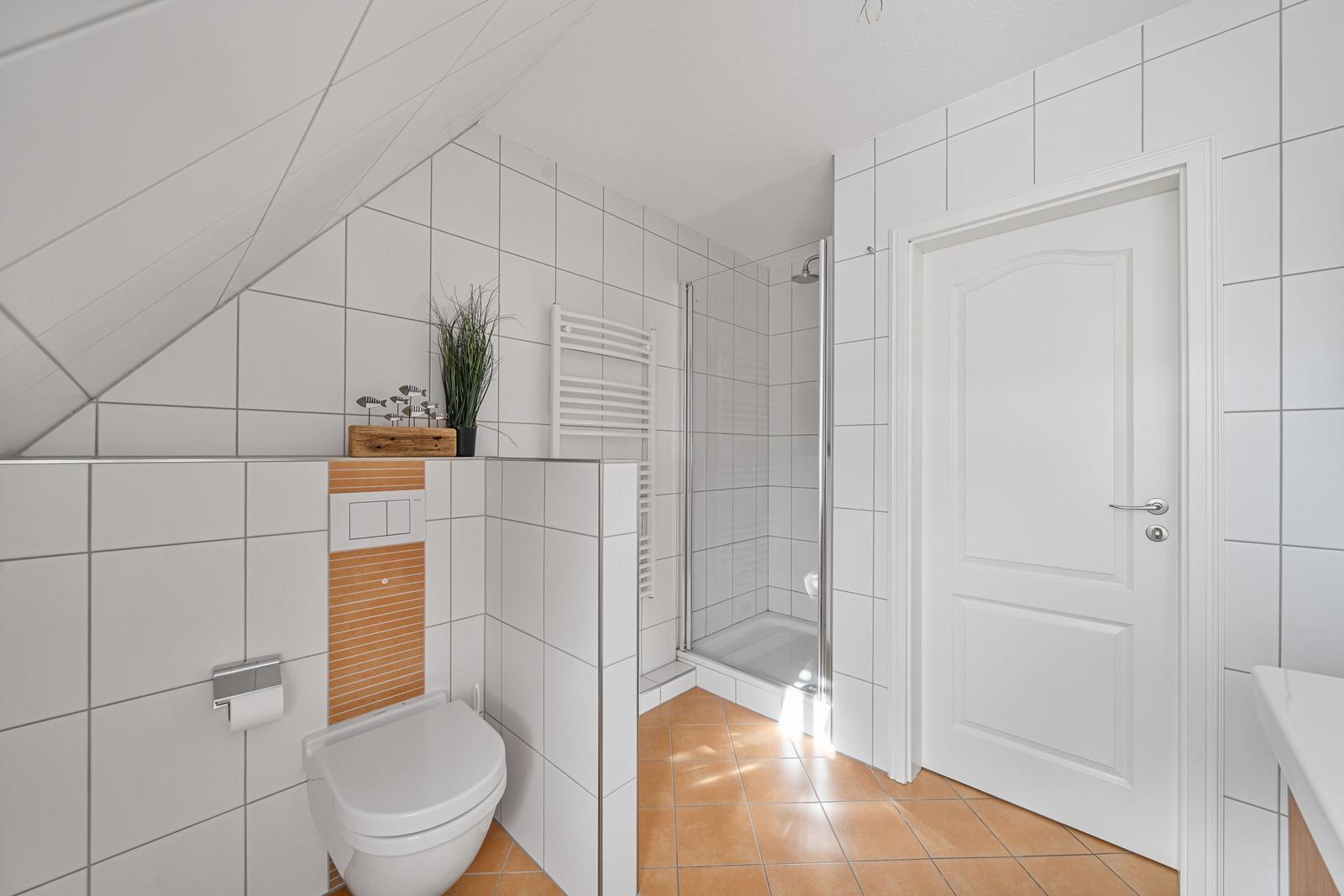 Badezimmer mit Dusche, Toilette und Waschbecken. Weiße Fliesen und Holzfußboden.