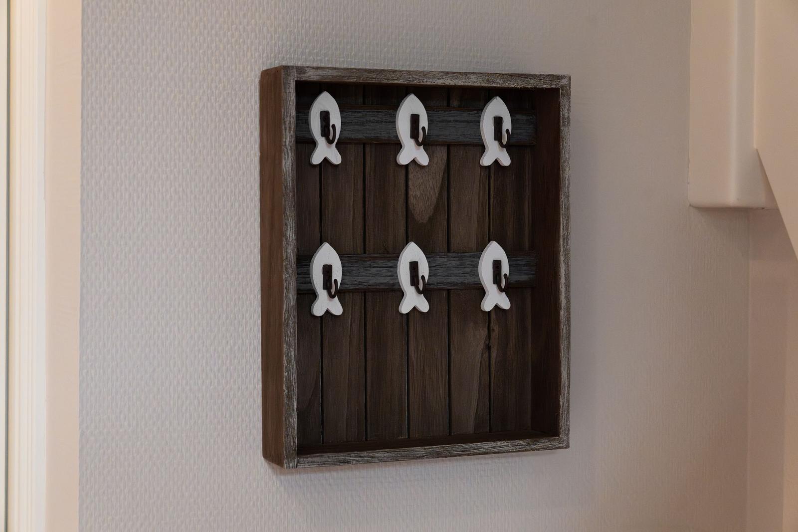 Wandhalter mit sechs weißen Fischform-Haken aus Holz an einer Wand.
