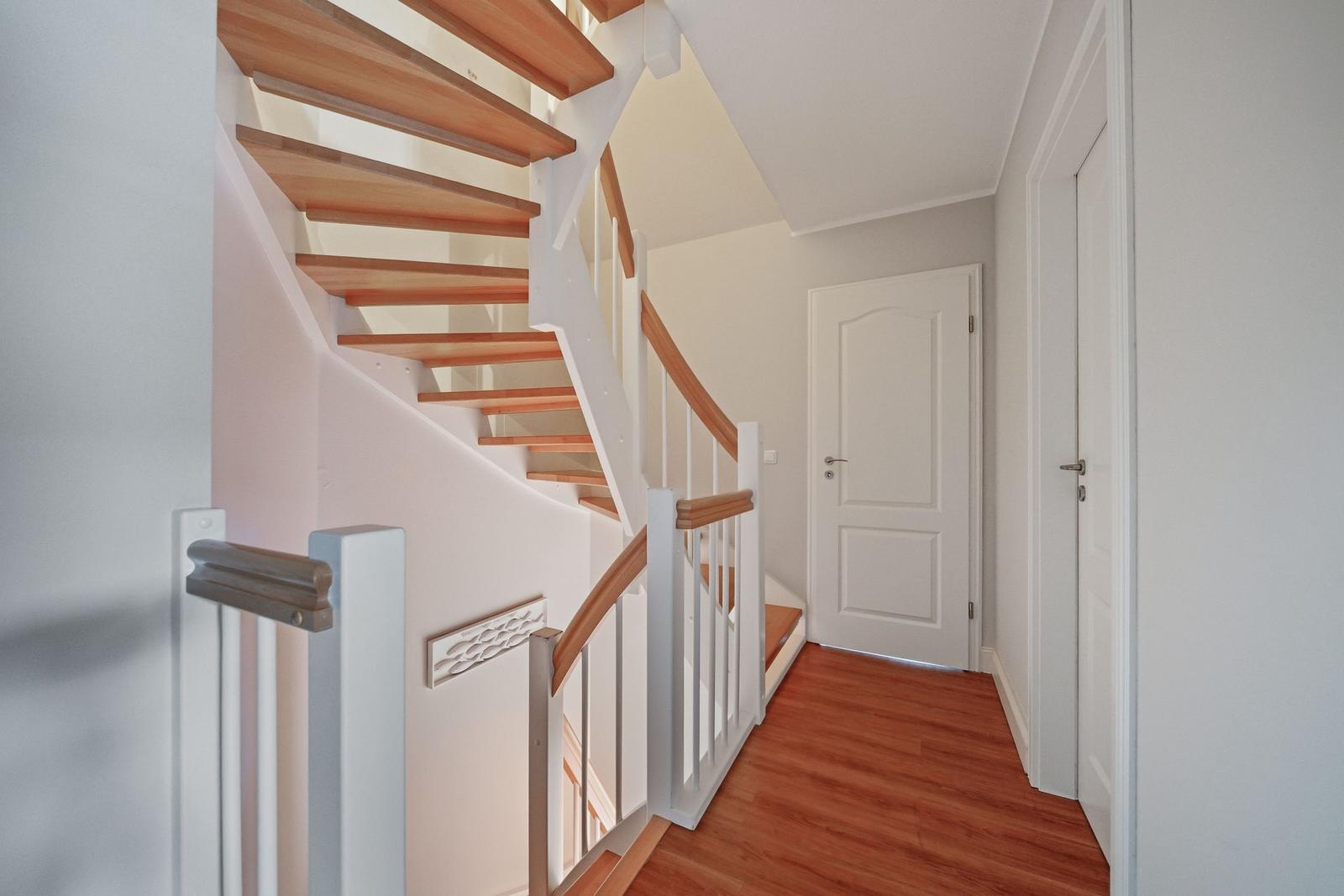 Haus mit Holztreppe und weißen Geländern. Flur mit Holzboden und Türen.