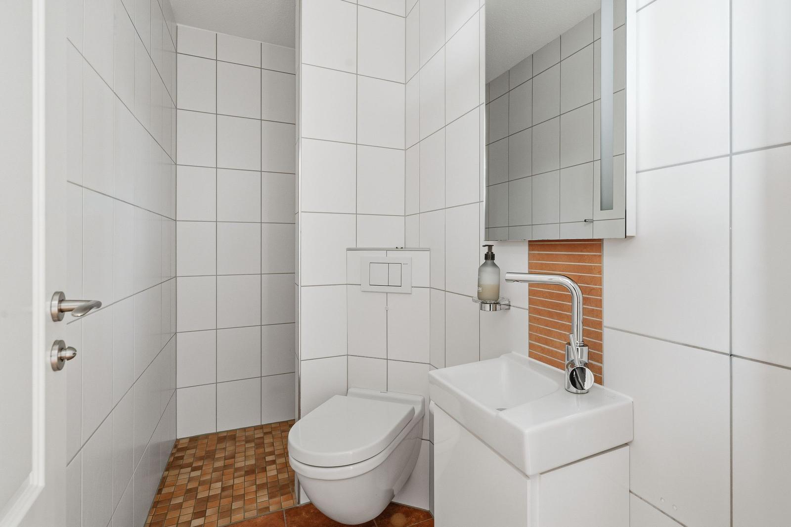 Badezimmer mit Toilette, Waschbecken und Spiegel. Wandfliesen und Bodenfliesen.