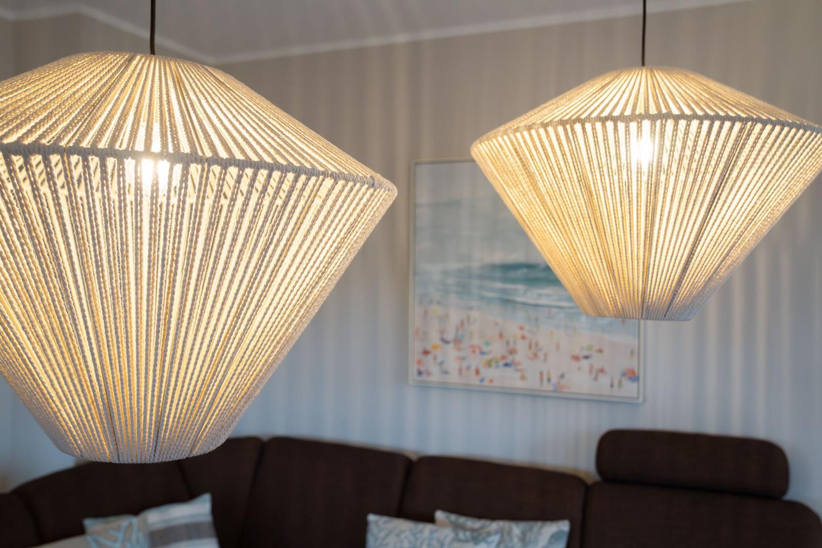Zwei hängende Lampen mit Seilrahmen über einem Sofa mit Kissen.
