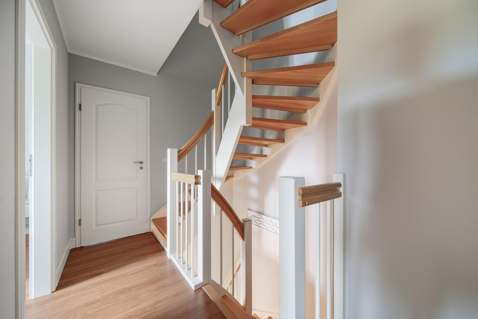 Helle Treppe mit Holzstufen und weißer Balustrade führt zur oberen Etage.