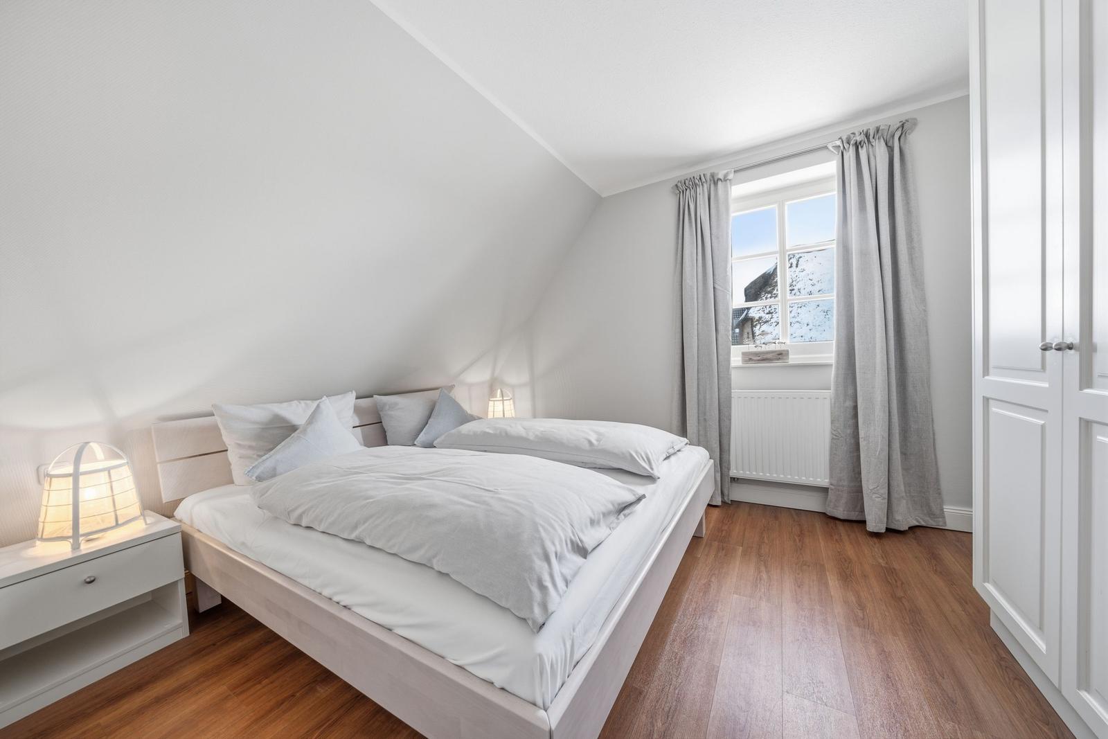 Schlafzimmer mit Bett, Nachttisch und Fenster mit Vorhängen.