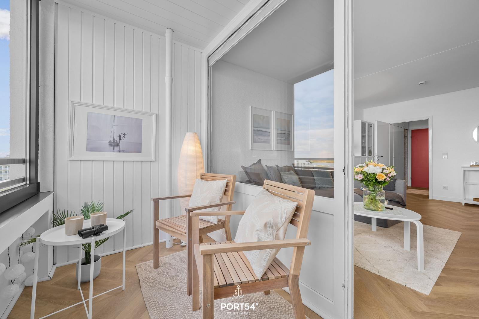 Terrasse mit zwei Holzstühlen, Tisch und Fensterblick. Blick ins Wohnzimmer mit Sofa und Blumen.