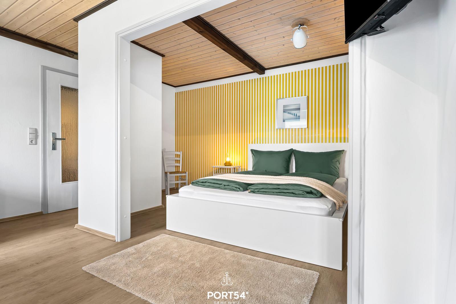 Schlafzimmer mit weißem Bett, gelber Wand und Holzdecke.