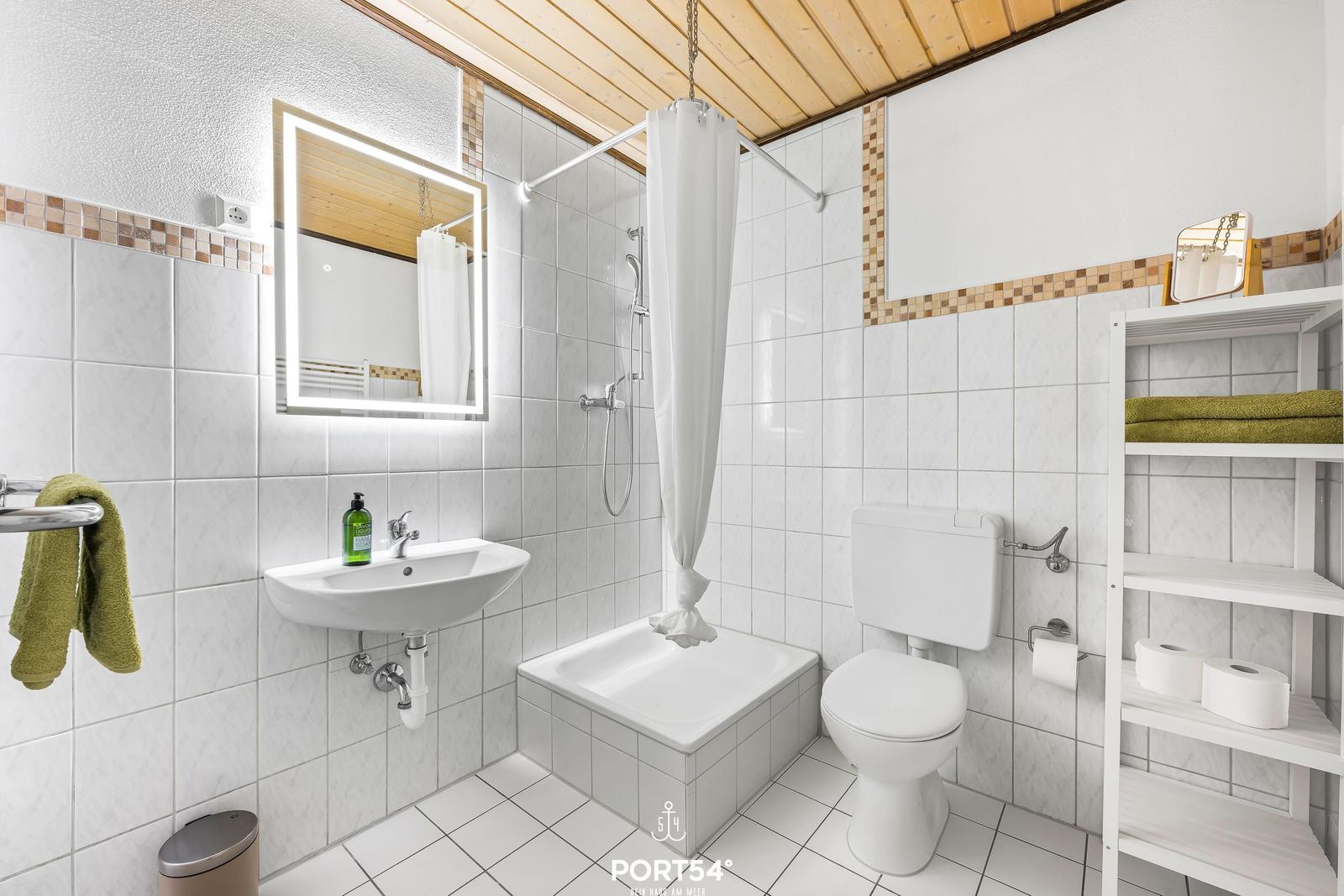 Badezimmer mit Dusche, Toilette und Waschbecken. Holzdecke und weiße Fliesen.