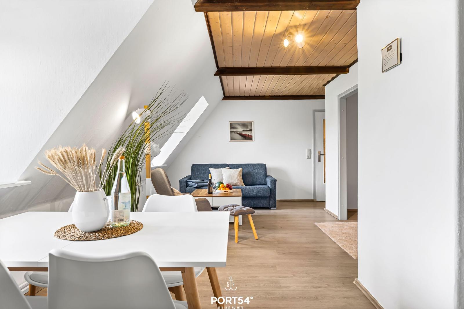 Dining area with white table and chairs. Living room with blue sofa and wooden ceiling.
